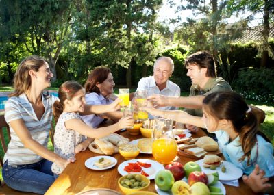 Family, including children (7-11) sitting at table in garden, toasting with orange juice and smiling