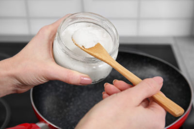 Woman putting coconut oil into frying pan